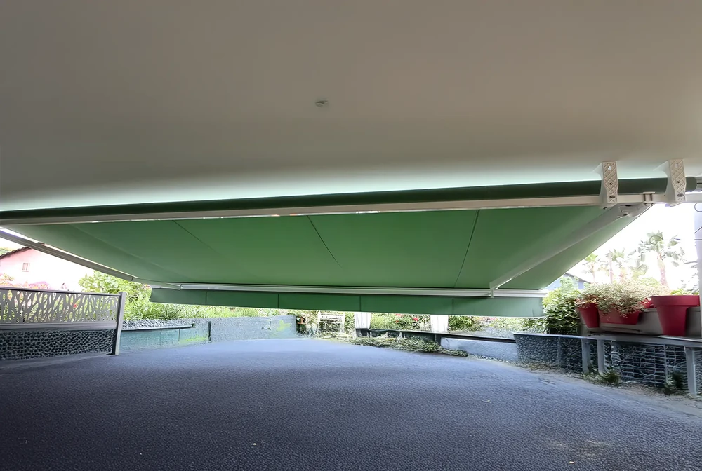 Terrasse couverte par store banne vert déployé, structure métallique apparente avec bras articulés