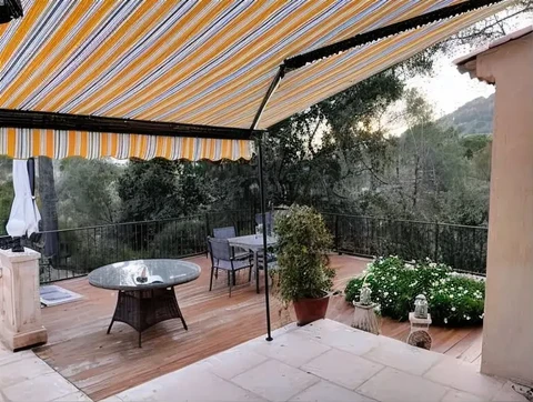 Terrasse extérieure aménagée avec store banne à rayures orange et blanc déployé au-dessus d'un salon de jardin