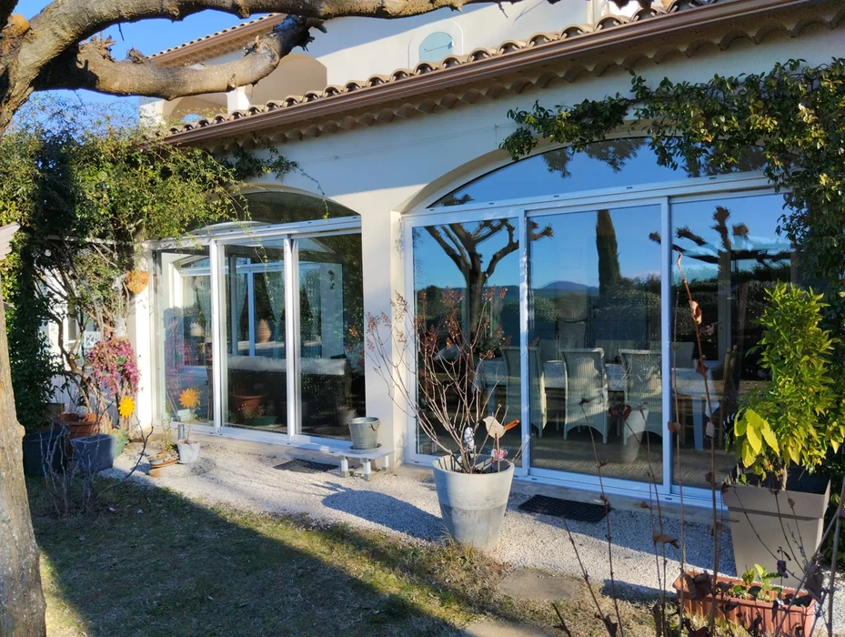 Véranda moderne avec structure aluminium blanc et verrière panoramique attenante à maison provençale