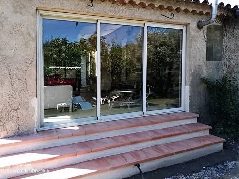 Terrasse extérieure d'une maison avec grande baie vitrée coulissante à trois vantaux en aluminium blanc