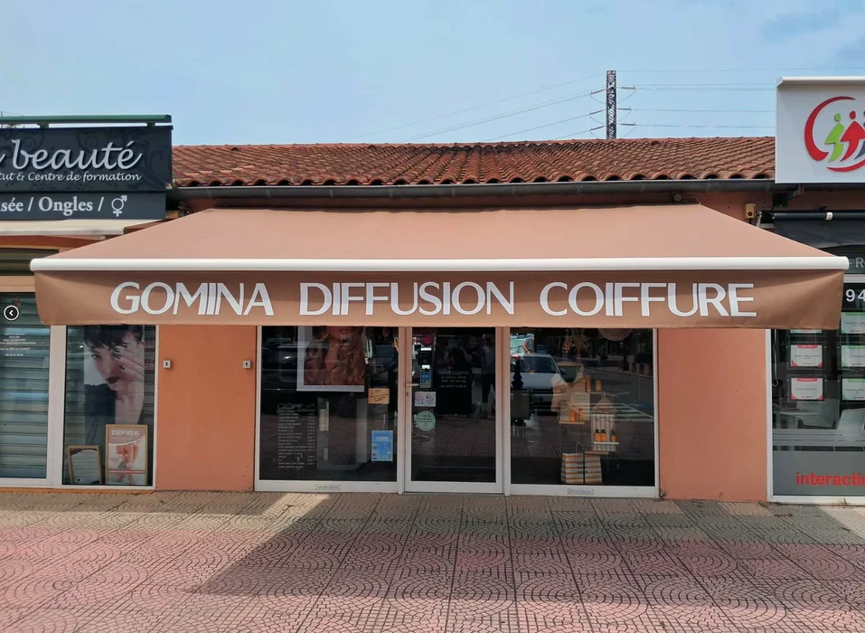 Devanture d'un salon de coiffure avec enseigne "GOMINA DIFFUSION COIFFURE" sur façade orange sous auvent beige