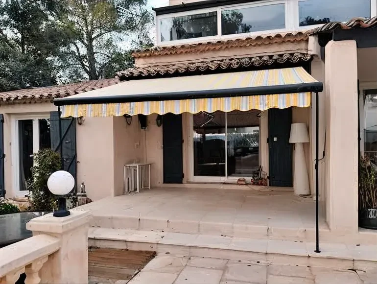 Terrasse extérieure d'une maison provençale avec store banne rayé jaune et blanc déployé au-dessus d'une zone couverte