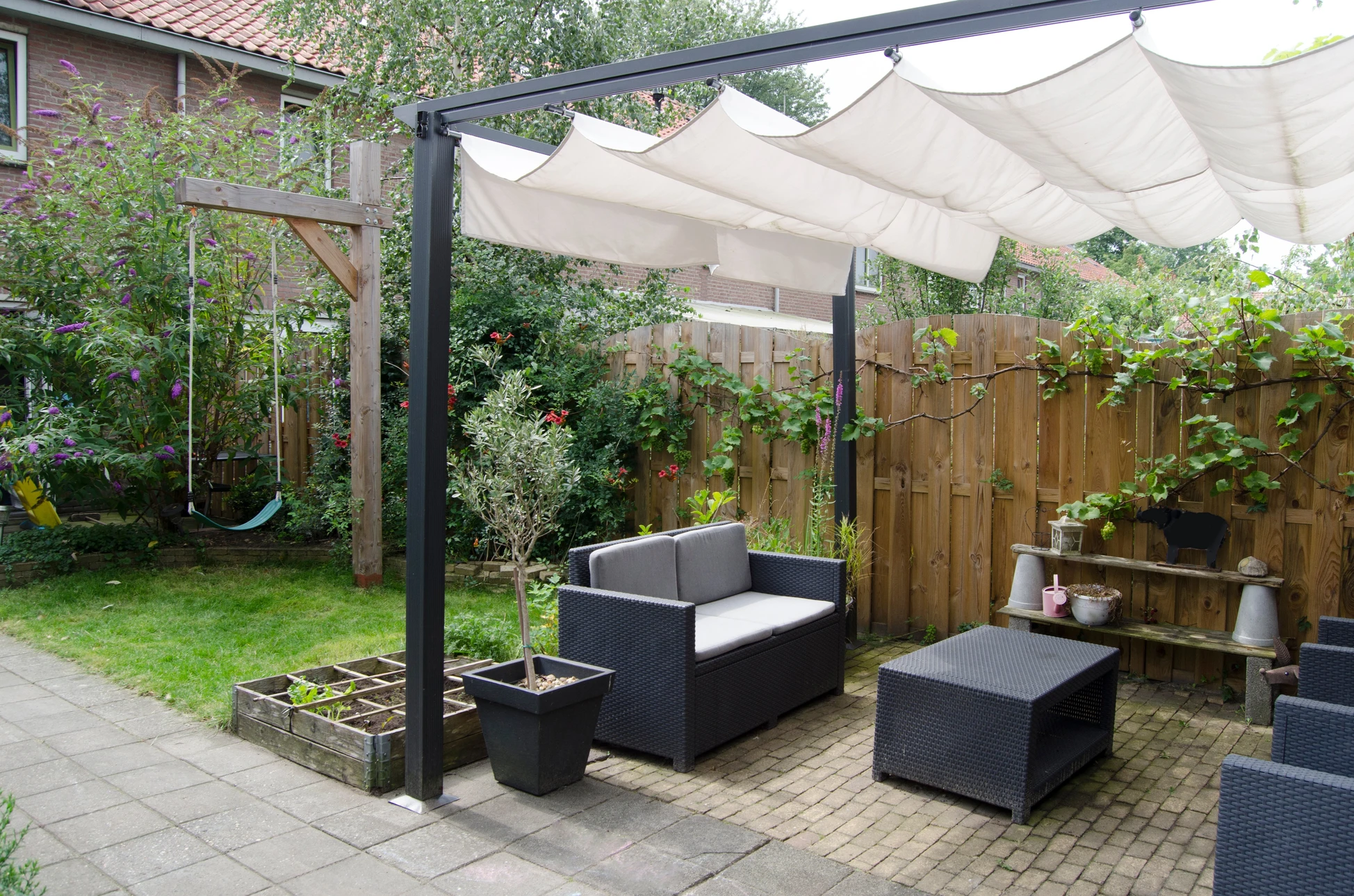 Jardin privé avec terrasse aménagée comprenant salon de jardin en résine tressée noire sous pergola avec toile d'ombrage beige